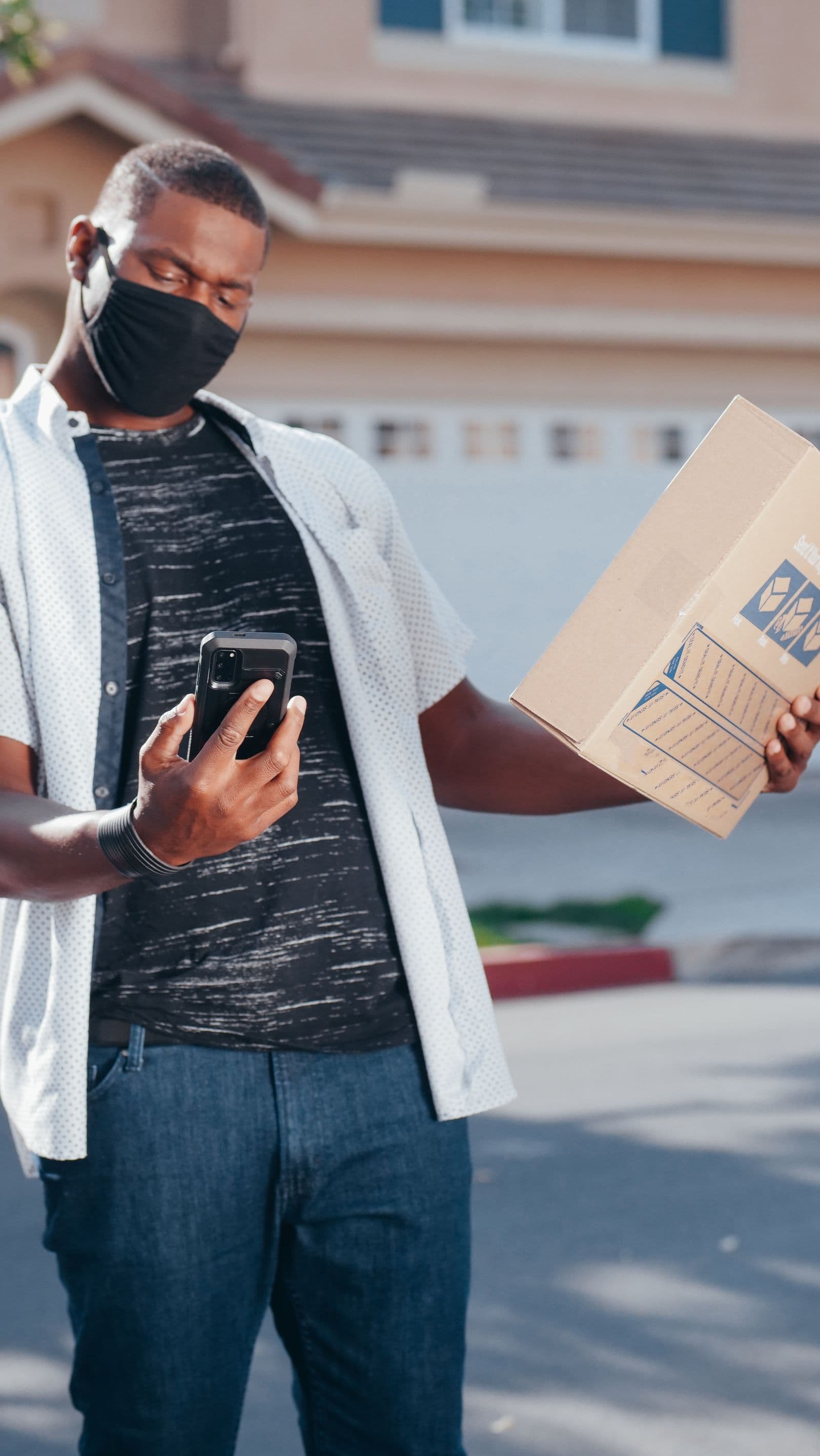 A courier checks a delivery status on a smartphone while holding a customer's parcel