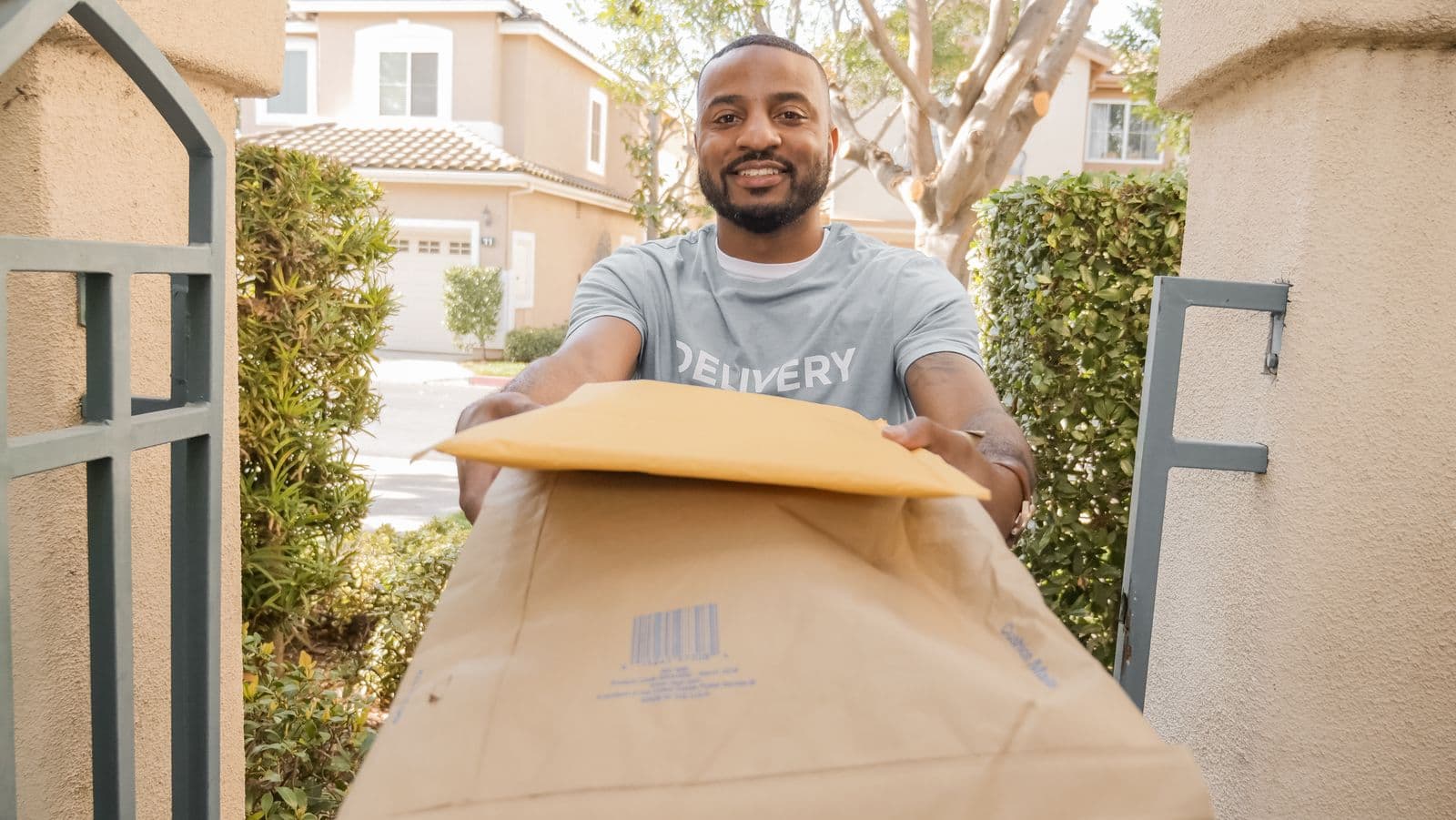 A smiling courier handing a package to a customer at their front gate