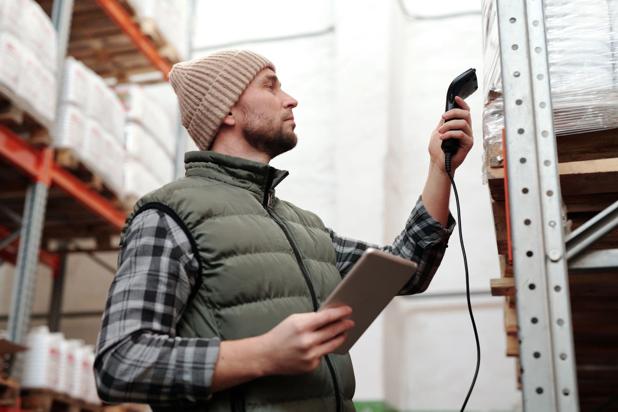 A warehouse worker scanning a package with a handheld barcode scanner while holding a tablet